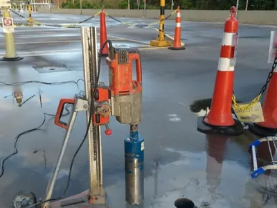 Perfuratriz diamantada executando furo em pista de concreto com sinalização de obra